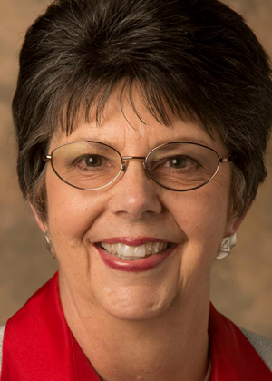 In an undated photo, Nancy Gwinn is seen smiling at the camera. She is wearing wire-framed glasses and a red shirt. 