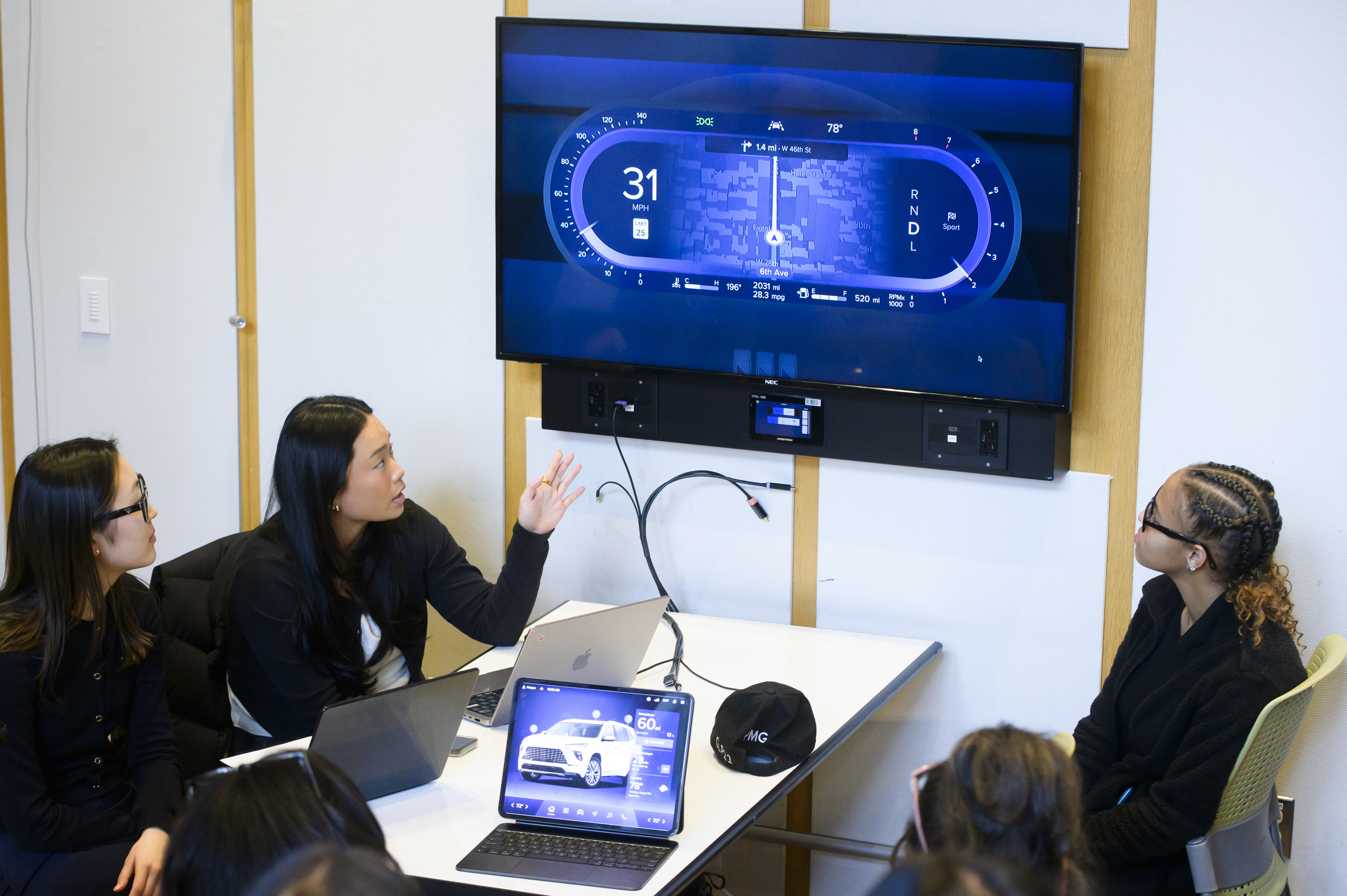 Students sitting at a table and looking at a screen showing data from a car.