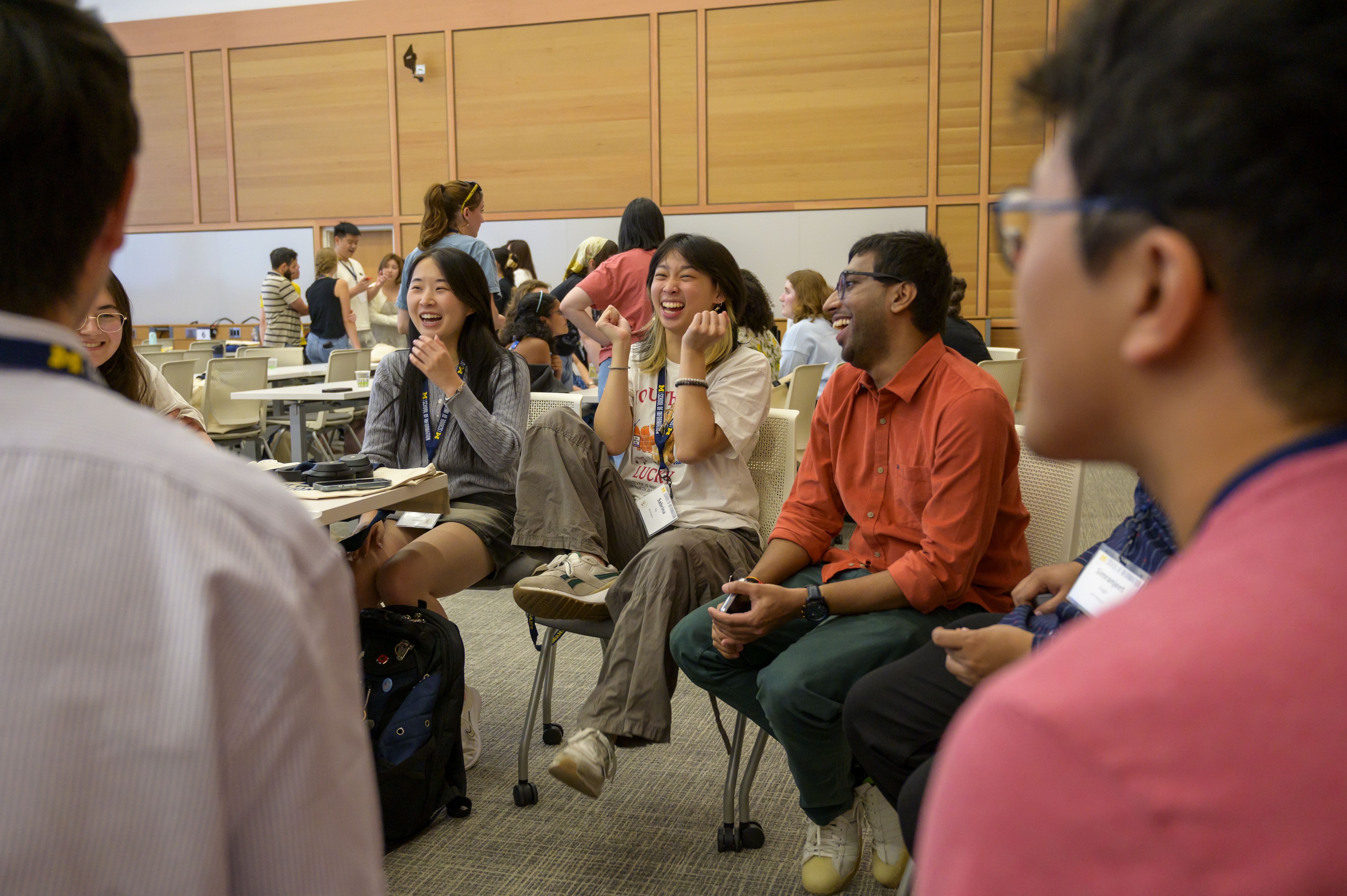 A small group of students sits in a circle in a large lecture hall, laughing and smiling.