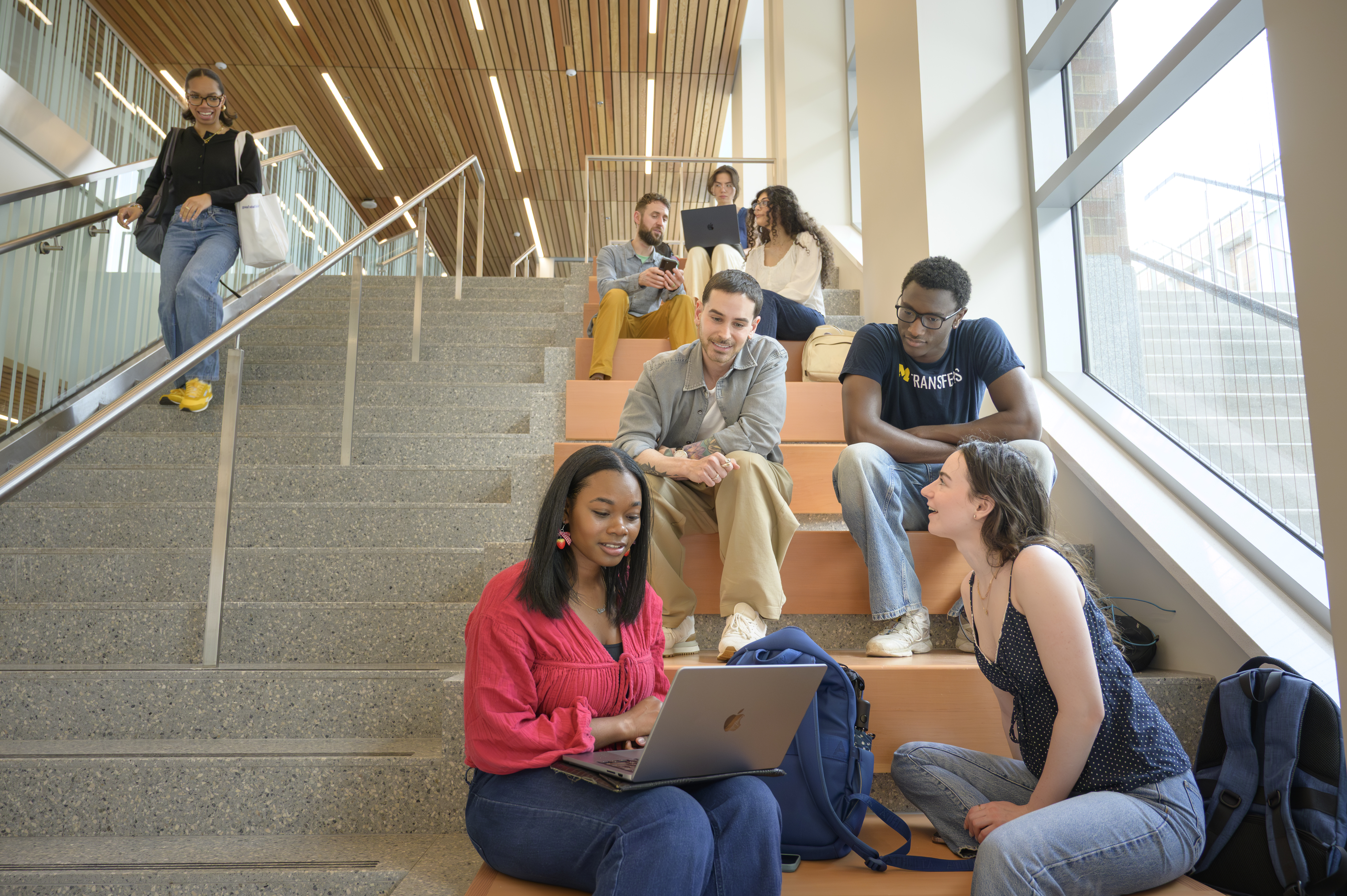 Masters students sit and talk on a main lobby stairwell in the Leinweber building.