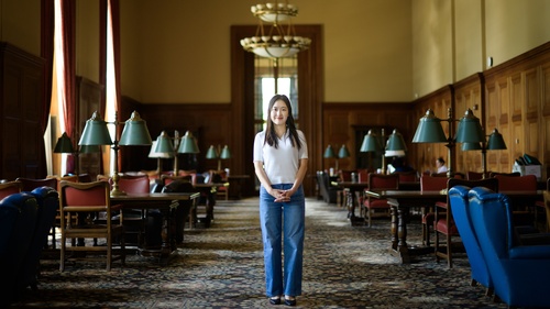 Jane Im stands in a carpeted room in Rackham with dark wood tables lining either side