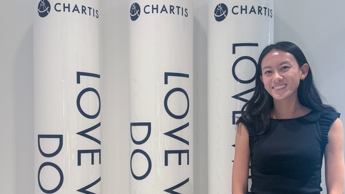 A student standing next to three pillars with the Chartis logo on them.