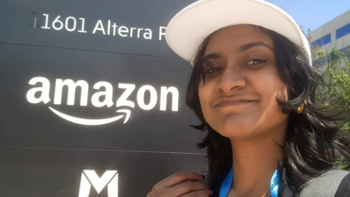 A student standing next to a sign with the Amazon logo on it.