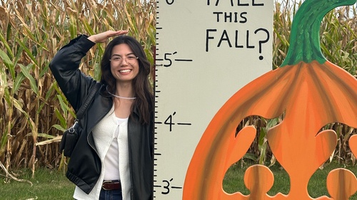 Chandra Behr standing in front of a corn field next to a board with foot markings on it. Chandra is about 5'5".