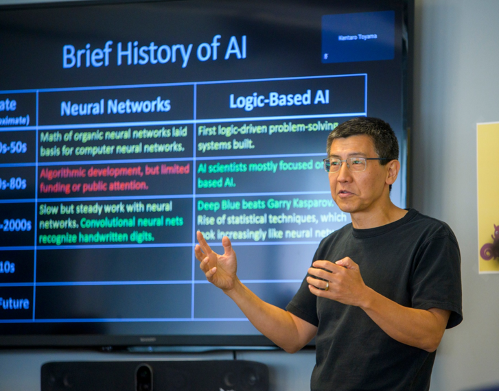 presenter standing in front of slide that lists a brief history of AI
