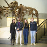 Four Bachelor of Science in Information Capstone students posing for a picture in the Museum of Natural History in front of a large dinosaur skeleton.