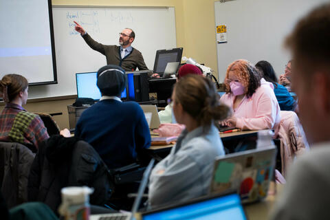 teacher standing in front of class pointing to a presentation screen