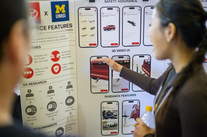 A student gestures toward a project poster with mockups of mobile designs.