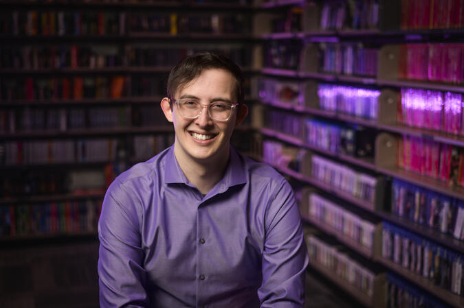 A headshot of Clayton Zimmerman taken in front of floor to ceiling bookshelves.
