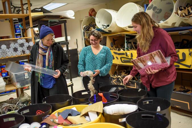 Three people sorting craft supplies in a room full of buckets.