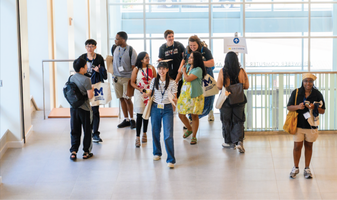 Students walking to and from a staircase in a building with floor to ceiling windows.