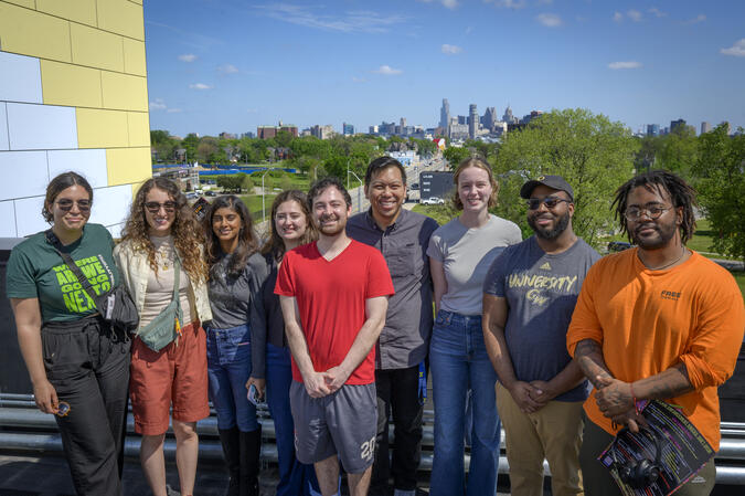 Eight students and Matt Bui pose on the rooftop of the LOVE Building with the Detroit skyline behind them