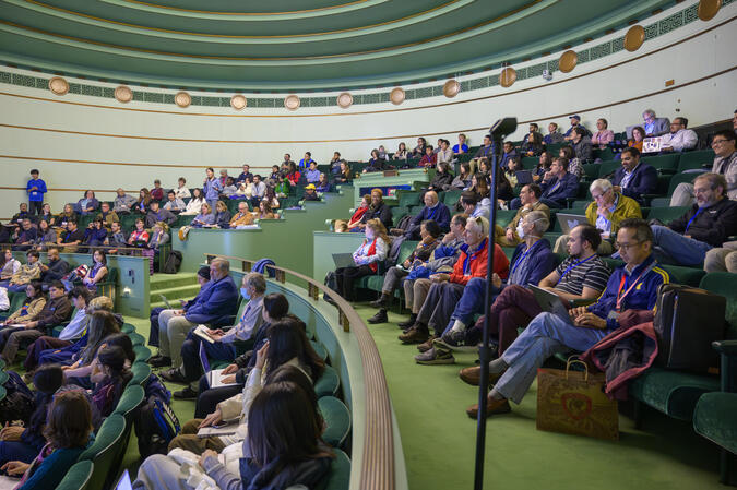A side view of a packed crowd seated in elevated rows in the seafoam green Rackham Amphitheatre