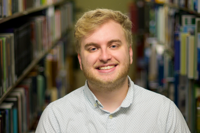 A headshot of Austin Book with library bookshelves in the background.