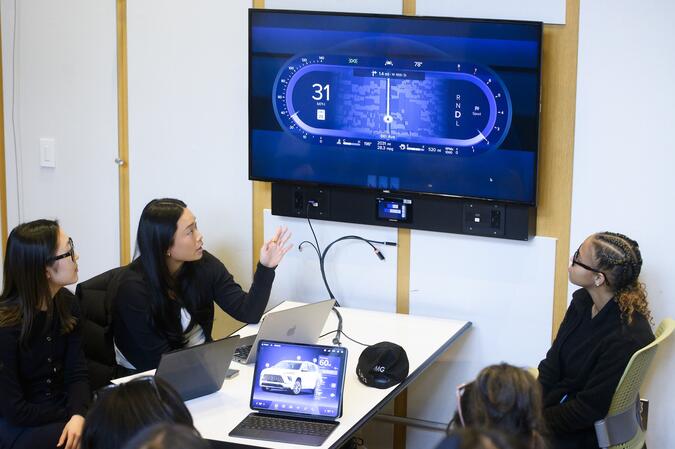 Students sitting at a table and looking at a screen showing data from a car.