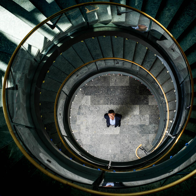 Overhead view of Kentaro Toyama standing at the center of a circular spiral staircase, looking up. 