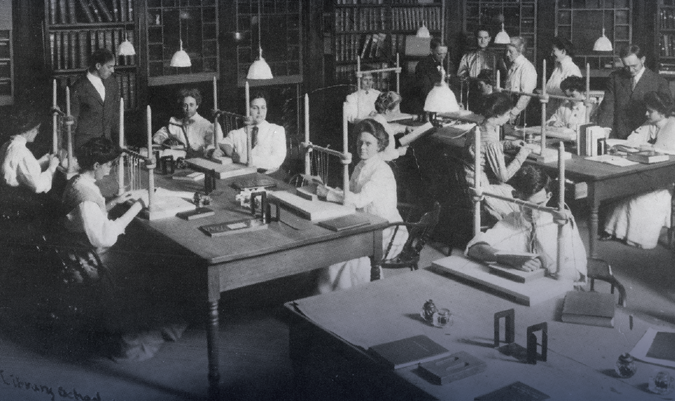A black and white photo of men and women working at desks