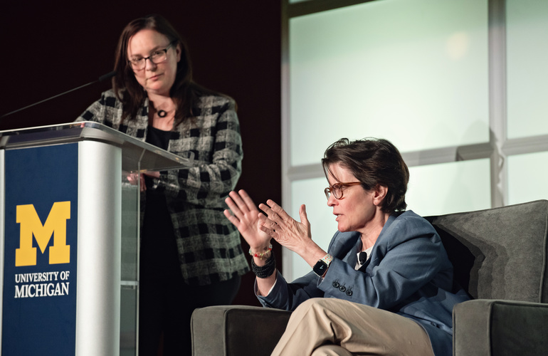 A photo with Kara Swisher talking on stage. Andrea Forte listens from behind a podium