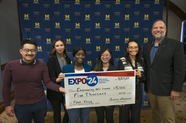 A group stands in front of a banner with UMSI logos holding a large check