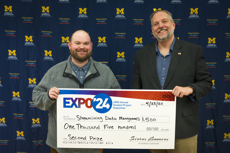 A group stands in front of a banner with UMSI logos holding a large check