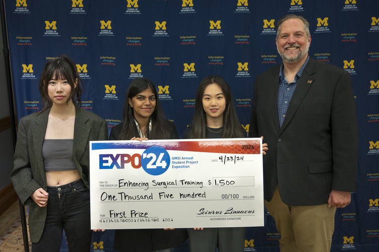 A group stands in front of a banner with UMSI logos holding a large check