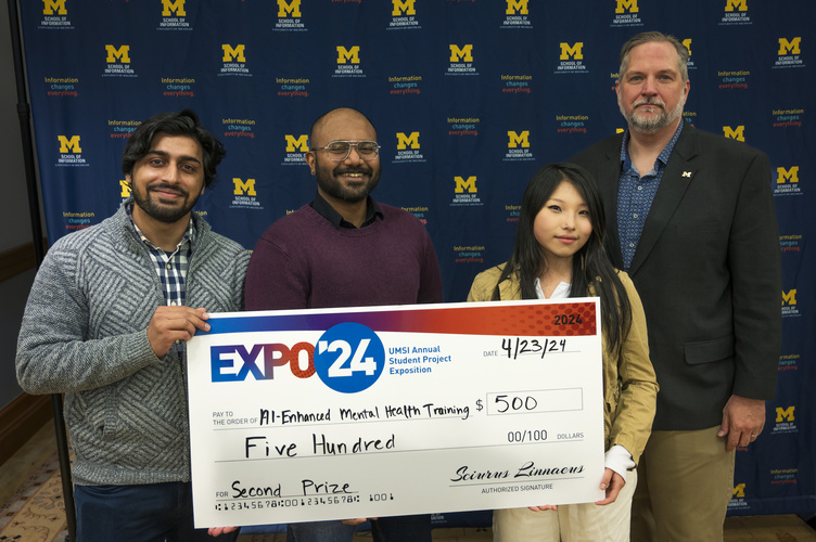 A group stands in front of a banner with UMSI logos holding a large check