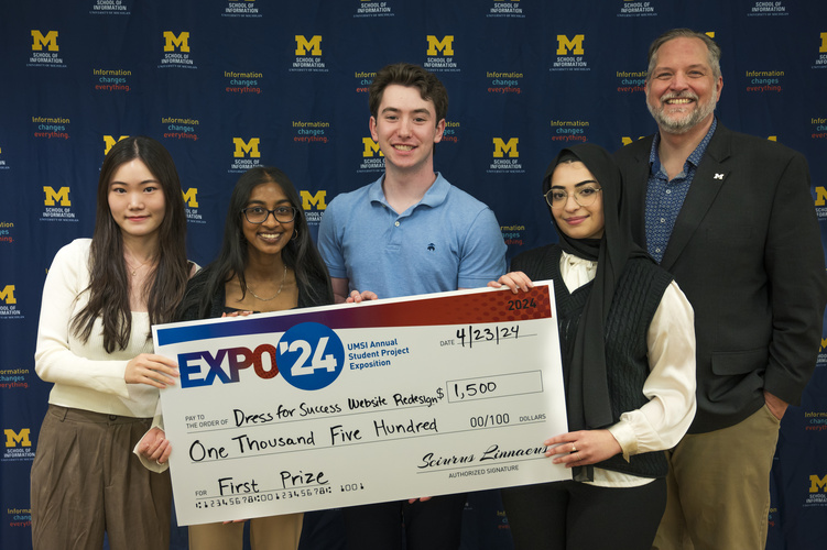 A group stands in front of a banner with UMSI logos holding a large check