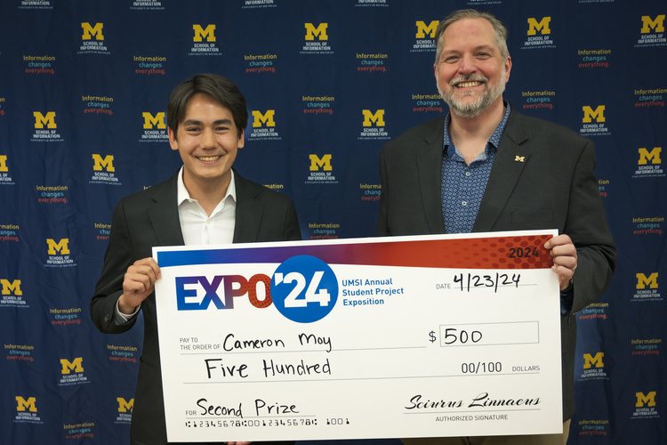 A group stands in front of a banner with UMSI logos holding a large check