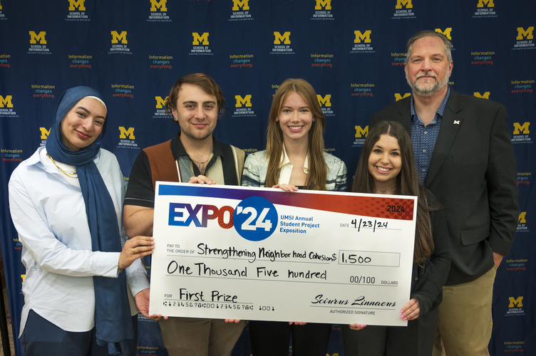 A group stands in front of a banner with UMSI logos holding a large check