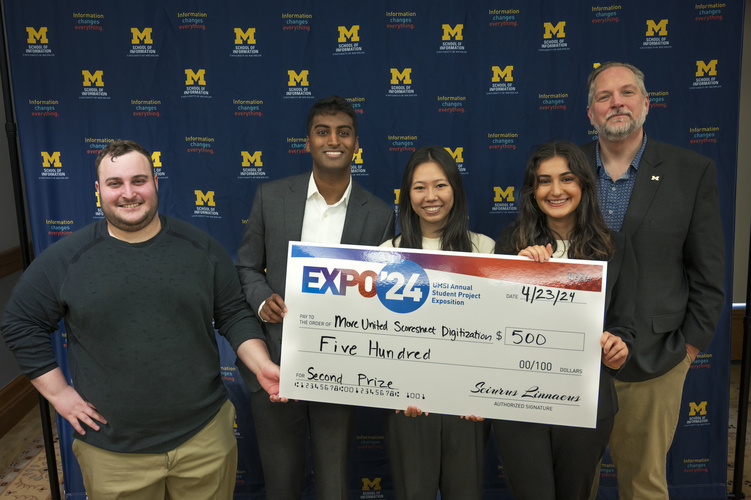 A group stands in front of a banner with UMSI logos holding a large check