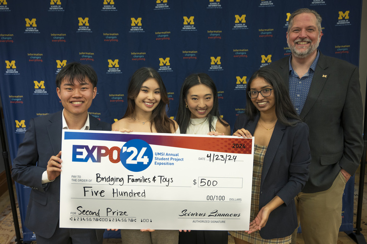 A group stands in front of a banner with UMSI logos holding a large check