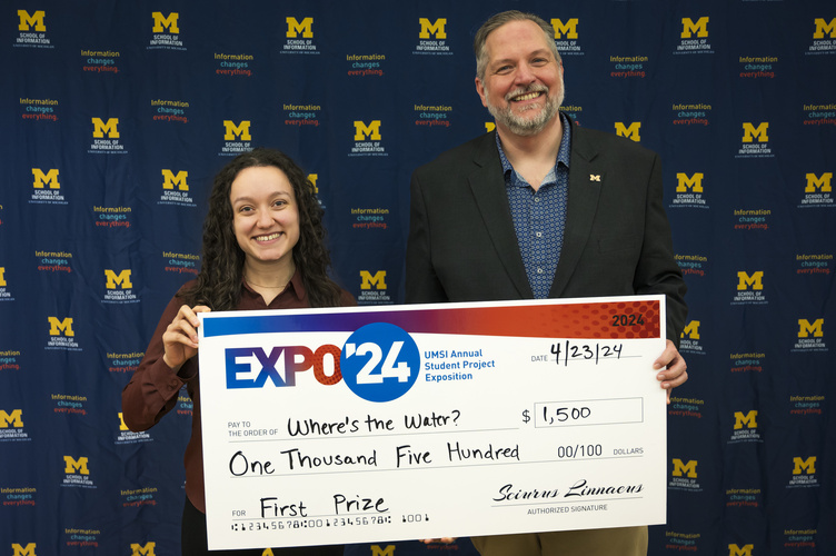 A group stands in front of a banner with UMSI logos holding a large check