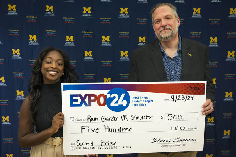 A group stands in front of a banner with UMSI logos holding a large check
