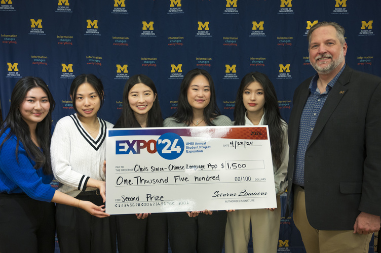 A group stands in front of a banner with UMSI logos holding a large check
