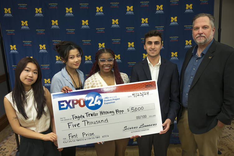 A group stands in front of a banner with UMSI logos holding a large check