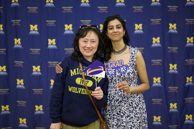Two MADS students pose for a photo with a step-and-repeat background featuring the UMSI logo