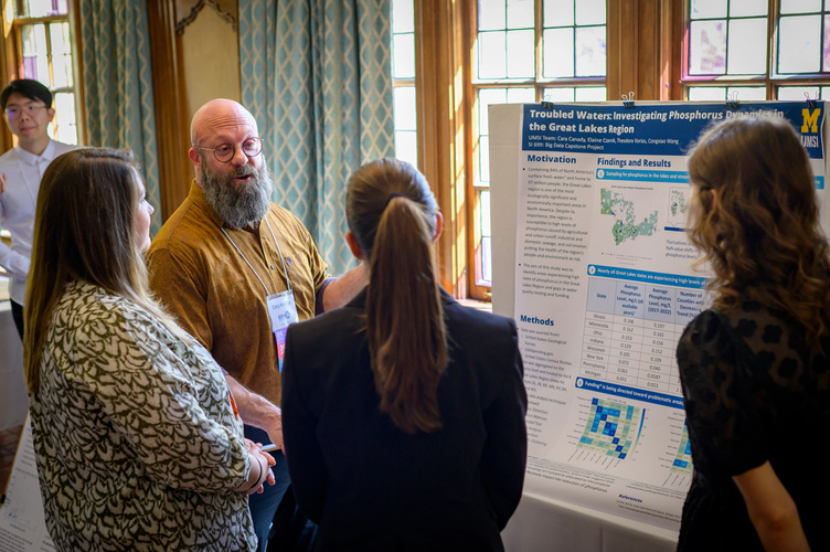 An Exposition judge speaks with three students in front of their trifold poster