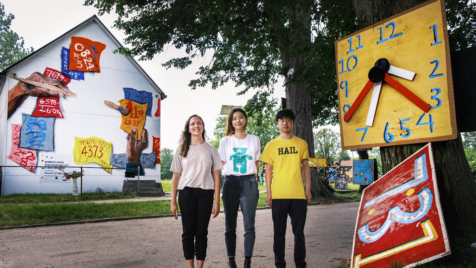 Students stand near large painted clocks on a Detroit street