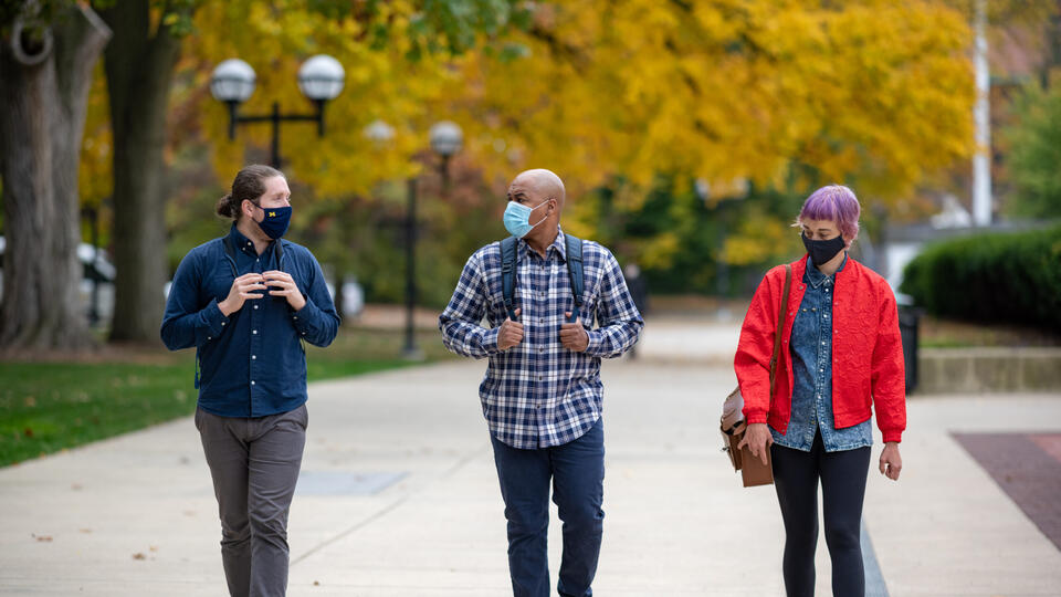 Three students walking on the University of Michigan campus and wearing masks
