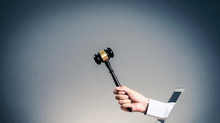 A hand holding a gavel coming out of a laptop screen