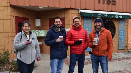MADS students Stacey Bruestle, Stephen Ontko, David Hernandez and Daniel Best holding to-go coffees outside a coffee shop