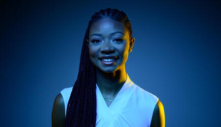 Shelby in black and blue light smiling at the camera and wearing a white shirt.