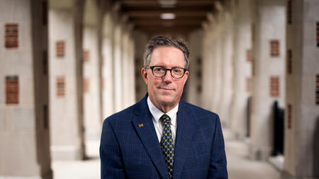 UMSI Dean Thomas A. Finholt standing beneath the arches in the North Quad courtyard