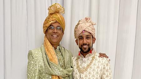 Father and son Nick and Ani Madurkar stand side by side wearing traditional Indian wedding clothing. 