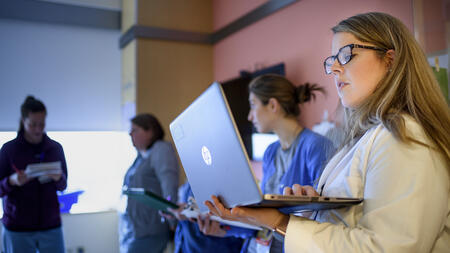 MHI student Emily Trumpower wearing a white lab coat and looking at a laptop. 