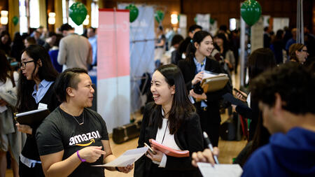 Students gathering at a UMSI career fair. One student smiles and talks with an Amazon employee. 