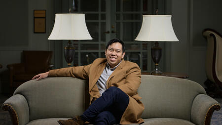 Matthew Bui sitting on a couch wearing a blazer and smiling. 