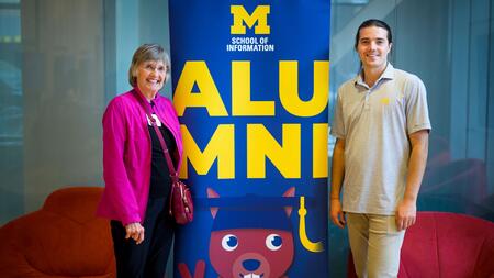 Two people stand next to a banner that says alumni
