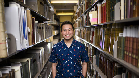 Ricky Punzalan smiling and standing in between two bookshelves. 