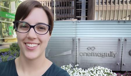 Maria Bronson in front of a OneMagnify sign.